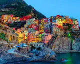 Case colorate aggrappate alla scogliera, un incantevole scorcio di quali sono le 5 Terre, con barche ormeggiate e il mare blu.