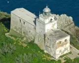 Faro abbandonato sull'isola di Palmaiola, con edifici in rovina e vegetazione rigogliosa che abbraccia la costa rocciosa.