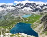 Laghi alpini blu e turchese ai piedi del Colle del Nivolet, con strade tortuose e montagne innevate sullo sfondo.