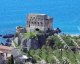Torre aragonese a picco sul mare, uno dei borghi da visitare in Calabria, con case e vegetazione lussureggiante.
