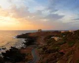 Torre di tramontana e case sparse su una collina, con mare e cielo al tramonto. Ecco cosa vedere a Ustica per un'esperienza indimenticabile.