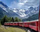 Treni panoramici rossi attraversano un paesaggio alpino mozzafiato con montagne innevate e foreste verdi.