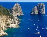 Faraglioni di Capri, tra le più belle isole di Napoli da visitare. Barche navigano nel mare blu intenso.