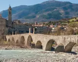 Ponte medievale in pietra attraversa un fiume, con un borgo storico e colline sullo sfondo. Un gioiello tra i borghi medievali dell'Emilia Romagna.