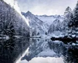 Val di Mello inverno: alberi innevati e montagne maestose si specchiano in un lago calmo, creando un paesaggio da fiaba.