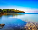 Torre medievale su una collina verdeggiante, con acque cristalline che lambiscono le **punta ala spiagge più belle**.