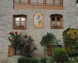 Un affresco sacro adorna un muro di pietra di un borgo trentino alto adige, con rose rosse che sbocciano rigogliose.