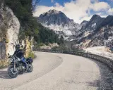 Motociclista su strada tortuosa con montagne di marmo sullo sfondo, un'autentica **Toscana da visitare**.