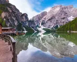 Il lago di Braies, Trentino, con le sue acque cristalline che riflettono le maestose montagne e i boschi circostanti. Una baita in legno e un pontile completano il paesaggio.