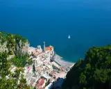 Vista dall'alto di Amalfi, con il mare blu e una barca a vela. La distanza tra Ravello e Amalfi è breve, ma il panorama è mozzafiato.