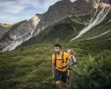 Coppia in escursioni alto adige, camminano su un sentiero verdeggiante con montagne imponenti sullo sfondo.