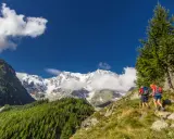 Due escursionisti affrontano un sentiero in Val d'Ossola, con maestose cime innevate sullo sfondo. Perfetto per escursioni facili.
