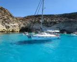 Catamarano "Respiro" in acque cristalline di un'isola sotto la Sicilia, con scogliere rocciose e altre barche.