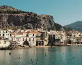 Un incantevole borgo da visitare in Sicilia, con case color pastello affacciate sul mare cristallino e una maestosa roccia a fare da sfondo.