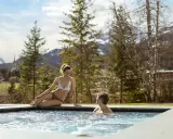 Coppia rilassata in una vasca idromassaggio all'aperto, con vista sulle montagne e sul paese, un'esperienza da provare alle terme Val di Fassa.