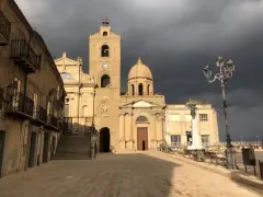 Piazza a Troina, dove si trova la maestosa cattedrale con il suo campanile e cupola, sotto un cielo minaccioso.