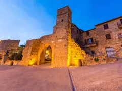 Antica porta e torre medievale illuminata, con case in pietra. Monticchiello cosa vedere: un borgo suggestivo.