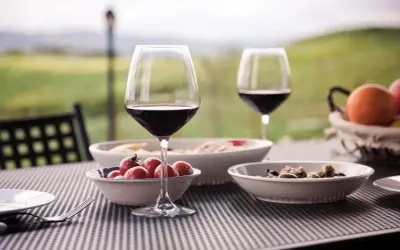 Un bicchiere di vino rosso e stuzzichini su un tavolo all'aperto, con un paesaggio collinare sullo sfondo, perfetto per un percorso enogastronomico toscana.