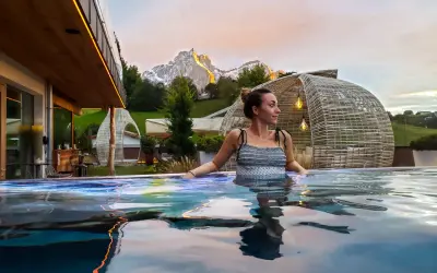 Donna rilassata in una piscina a sfioro con vista sulle montagne illuminate al tramonto, un'esperienza di benessere nelle terme in Trentino Alto Adige.
