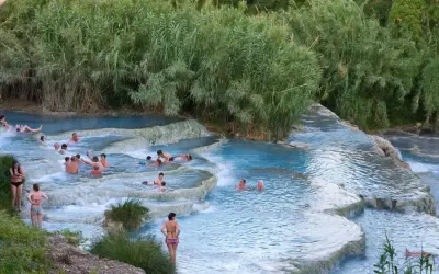 Persone si rilassano nelle cascate naturali delle terme famose in Italia, circondate da vegetazione lussureggiante.