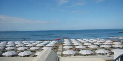 Spiaggia di **Marina di Follonica** con file ordinate di ombrelloni bianchi, mare azzurro e cielo sereno.
