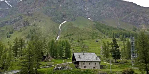 Un casolare in pietra nel **Val di Rhemes**, circondato da verdi pendii e imponenti montagne innevate.