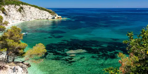 Scogliera bianca a picco sul mare cristallino della Toscana. Un angolo di paradiso con acque turchesi e vegetazione mediterranea.