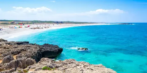 Scogli vulcanici e sabbia bianca su una spiaggia pop corn in Sardegna, con acque turchesi cristalline.