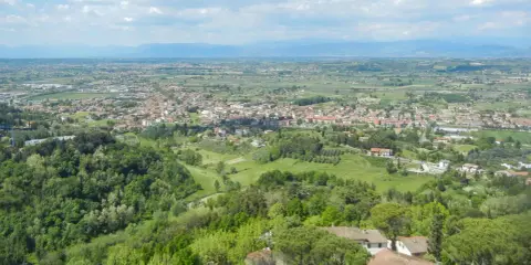 Panoramica di San Miniato Alto con colline verdi, case con tetti rossi e un cielo nuvoloso.