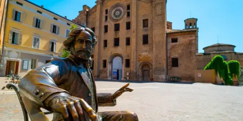 Statua di bronzo in piazza, con edifici storici sullo sfondo. Un assaggio delle città più belle Emilia Romagna.
