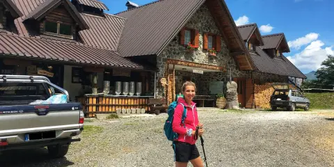Ragazza con zaino e bastoncini da trekking davanti a un rifugio alpino, una delle tipiche malghe in Friuli.
