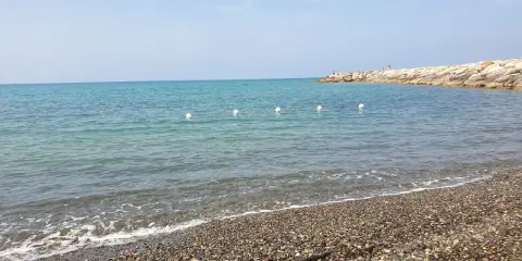 Spiagge più belle della Marina di Cecina: mare azzurro, ciottoli levigati e un molo roccioso con qualche bagnante.