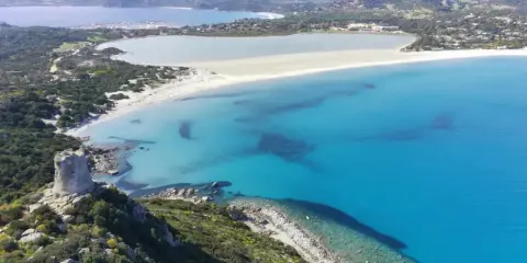Torre costiera su promontorio verdeggiante domina una baia con acque cristalline, tra le spiagge più belle Sardegna.