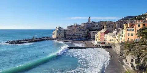 Colorati borghi medievali vicino a Genova, con onde turchesi che si infrangono sulla spiaggia di ciottoli.