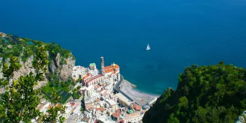 Vista dall'alto di Amalfi, con il mare blu intenso e una barca a vela. Il percorso da Amalfi a Ravello offre panorami mozzafiato.