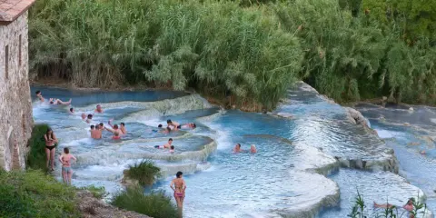 Persone si rilassano nelle cascate naturali delle terme famose in Italia, circondate da vegetazione lussureggiante.