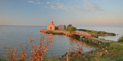 Un'isola con casette e un ponte di legno nei laghi dell'Emilia Romagna, al tramonto.
