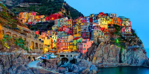 Case colorate aggrappate alla scogliera, un incantevole scorcio di quali sono le 5 Terre, con barche ormeggiate e il mare blu.