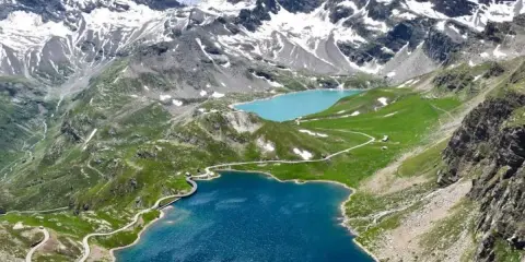 Laghi alpini blu e turchese ai piedi del Colle del Nivolet, con strade tortuose e montagne innevate sullo sfondo.