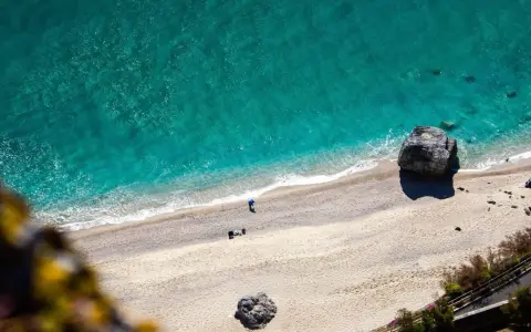 Spiaggia dorata e mare cristallino sulla riviera ligure di ponente. Un pescatore solitario e rocce imponenti.