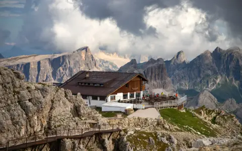 Rifugio alpino con terrazza panoramica, uno dei migliori rifugi dove dormire Dolomiti, incastonato tra imponenti vette rocciose e nuvole minacciose.