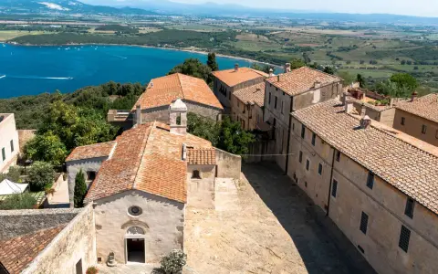 Vista dall'alto del populonia centro storico, con case dai tetti rossi e il mare blu sullo sfondo.