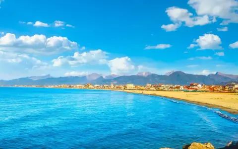 Spiaggia dorata e mare azzurro a Viareggio, con montagne sullo sfondo. Perfetto per scoprire cosa vedere a Viareggio in un giorno.