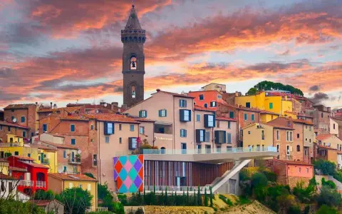 Un borgo italiano con case colorate e una torre campanaria, sotto un cielo infuocato. Potrebbe essere qual è il borgo più bello d'Italia.