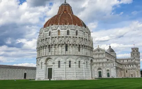 Il Battistero, il Duomo e la Torre Pendente: ecco cosa vedere a Pisa in un giorno, un'iconica piazza con un prato verde e cielo nuvoloso.