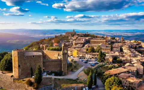 Un borgo medievale arroccato su una collina, tra i più belli d'Italia, con un castello imponente e case in pietra sotto un cielo azzurro.