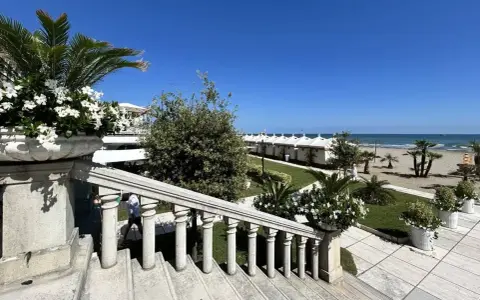 Scalinata in pietra con vasi fioriti, vista su una spiaggia ordinata con cabine bianche, tipica di una città di mare veneto.