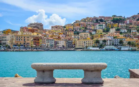 Panoramica di Porto Santo Stefano con case colorate a picco sul mare turchese. Un invito a scoprire cosa vedere a Porto Santo Stefano.