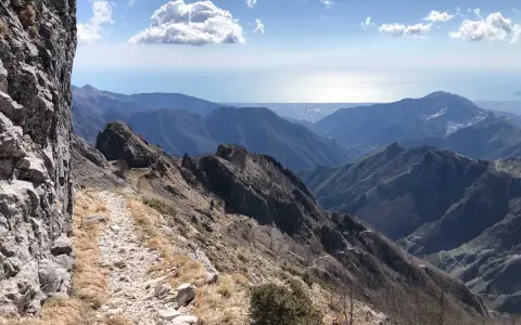 Sentiero roccioso su un crinale montuoso, con vista sul mare e sulle colline. Un percorso che ricorda la via Vandelli, un'antica strada panoramica.