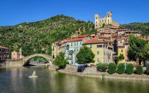 Borghi entroterra ligure levante: un ponte antico attraversa un fiume, case colorate si affacciano sull'acqua, un castello domina la collina verde.